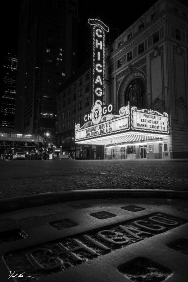 Black and white image of the historic Chicago Theater with a city sewer cap in the foreground with Chicago on it 