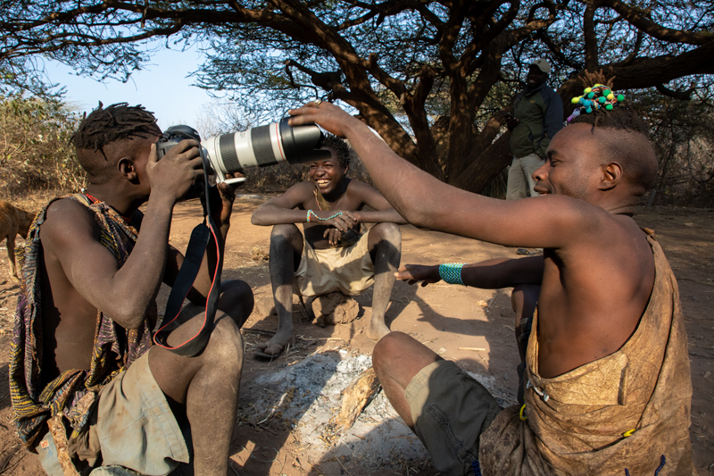 photo of Hadzabe tribe members playing with photographer Derek Nielsen's camera in Africa