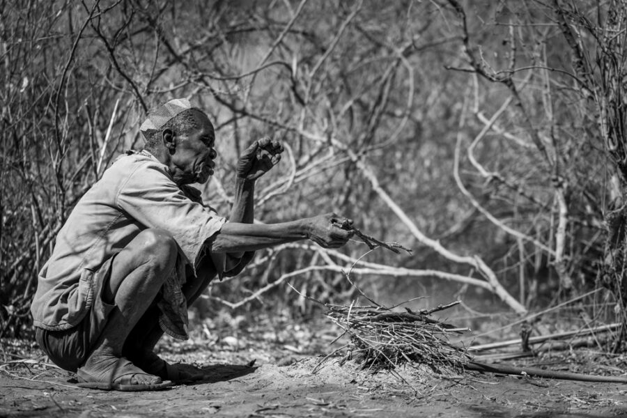 elder tribal member keeping warm over a fire in Tanzania