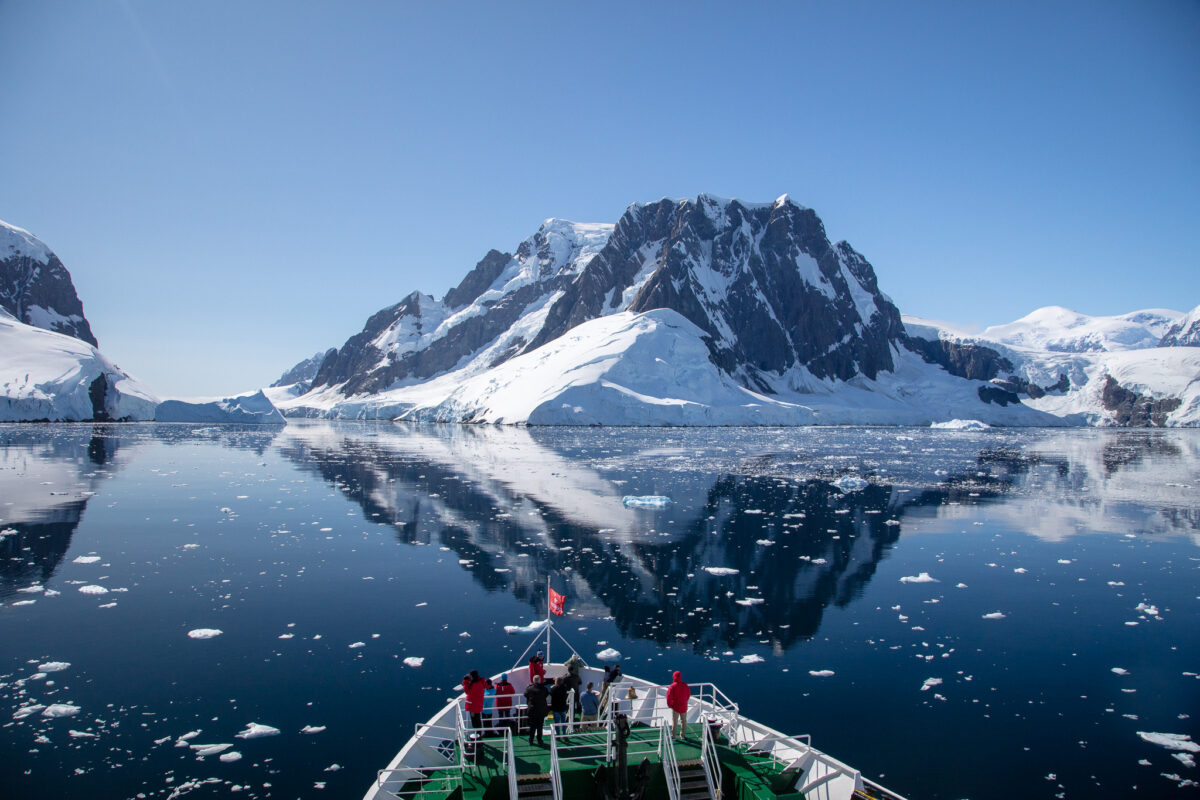 Photo of the Lamar Channel in Antarctica reflecting the mountains and the bow of the MS Expedition ship is at the bottom of the frame