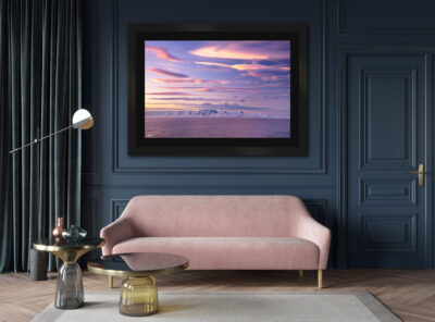 Large dark framed fine art print of a sunset over Antarctica with pink clouds displayed in the living room of a modern luxury home