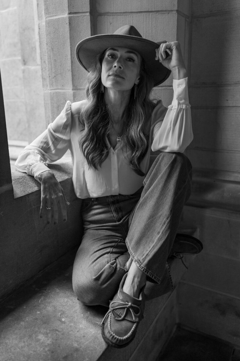 model with hat sitting by a window for a personal brand shoot