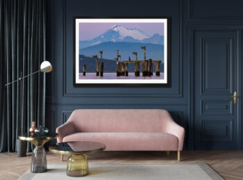 Large framed fine art print of a snow-capped mountain over the ocean displayed in the living room of a modern home