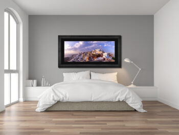 Large framed fine art print of Oia in Greece displayed in a bedroom of a modern home