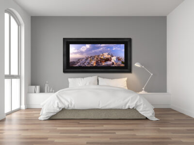 Large framed fine art print of Oia in Greece displayed in a bedroom of a modern home