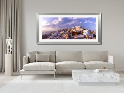 Large framed fine art print of Oia in Greece displayed above a couch in a modern luxury living room.