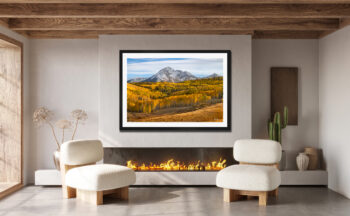 Large framed fine art print of a mountain in colorado during fall displayed above the fire palce in the living room of a modern home