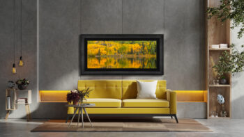 Large framed fine art print of golden trees in the mountains reflecting on a lake displayed above a couch in a modern home