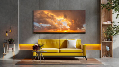 Large unframed fine art print of a sunset over the farms of the midwest united states displayed above a couch in a modern home