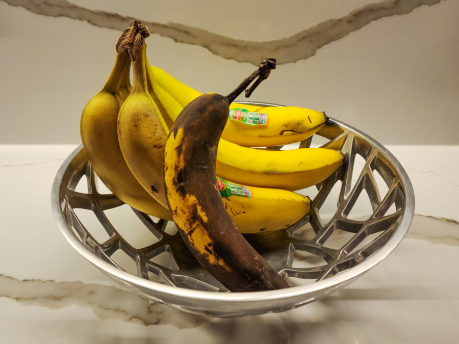 photograph of a bowl of bananas with one starting to spoil