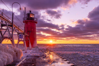 Vibrant sunset in South Haven, Michigan, with the red lighthouse in the foreground during winter